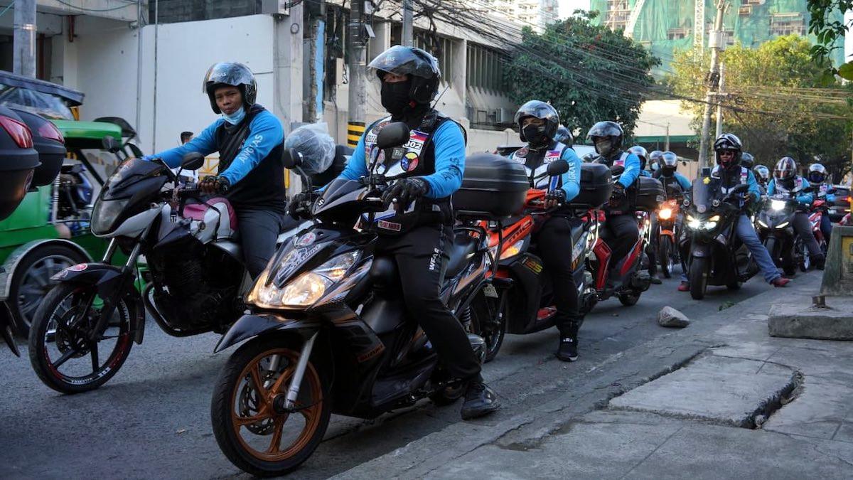 A group of motorcycle taxi drivers are waiting for passengers while seated on their motorbikes, wearing protective gear and the image represents the search query 'HP with longlasting battery for busy motorcycle taxi drivers'.
