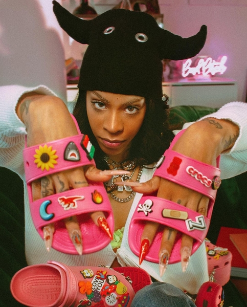 Rico Nasty holding up a pair of Crocs sandals