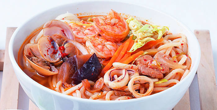 korean spicy seafood noodles topped with shrimp, shellfish, and veggies in a white bowl