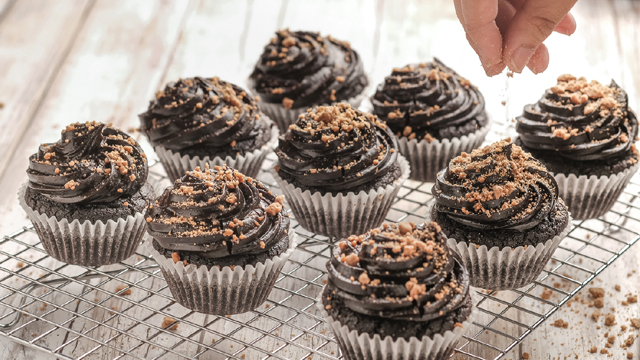 Double chocolate and peanut butter cupcakes being sprinkled with peanuts