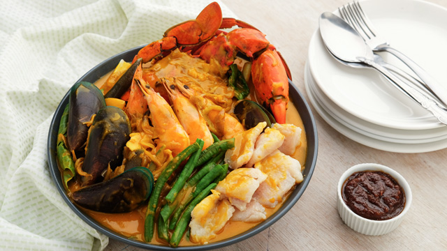 seafood kare-kare in a big black clay pot, topped with crab, mussels, prawns, and cream dory