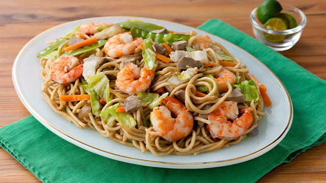 pancit canton topped with shrimp, cabbage and carrot slices, and snow peas