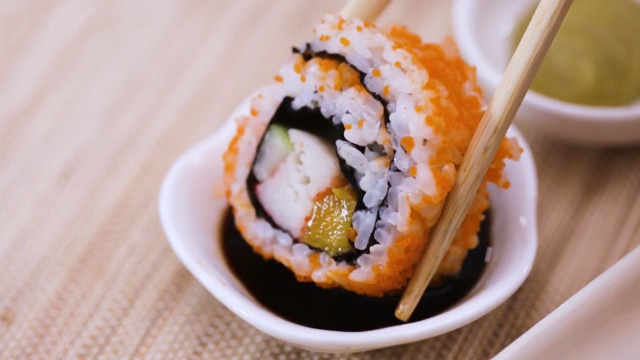 a piece of california maki being dipped in soy sauce