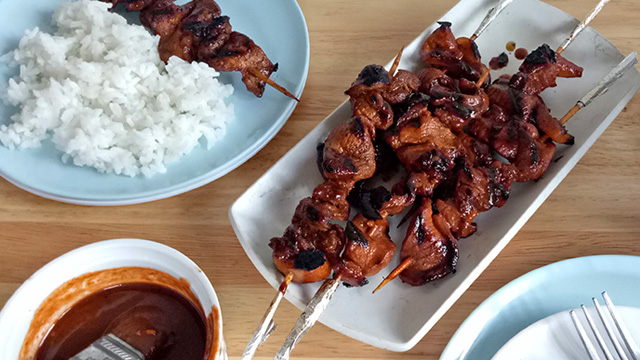 Filipino pork barbecue on a rectangular serving platter surrounded by blue plates that have rice and barbeque on them