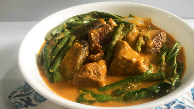 kare-kare made with beef chunks, sitaw, and bok choy in a white serving bowl