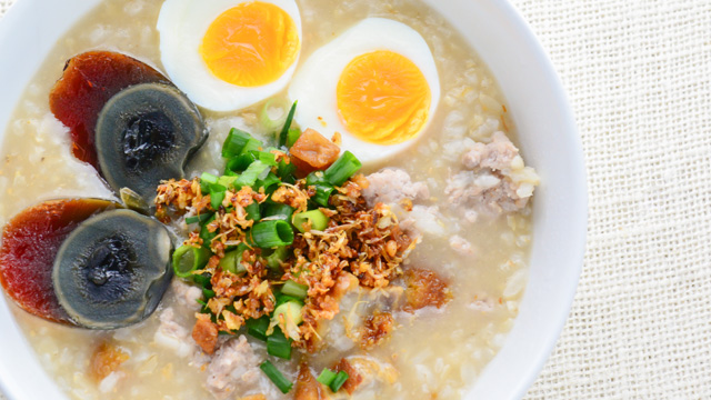 lugaw or congee topped with toasted garlic, chopped onions, sliced hard boiled eggs and century eggs