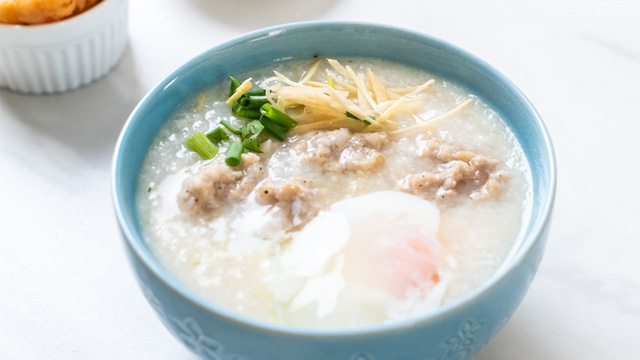 lugaw or congee with egg, chicken, and ginger slices in a light blue bowl