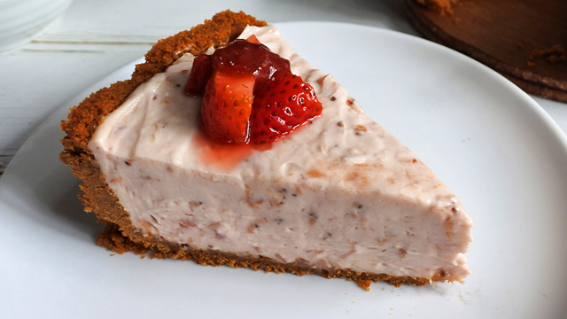 slice of strawberry cheesecake topped with macerated strawberries on a white plate