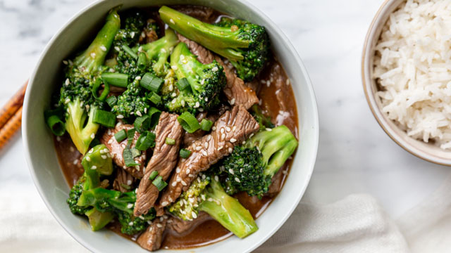 stir-fried beef broccoli in a big serving bowl, with another bowl of rice to the side