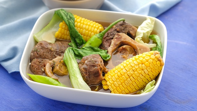 A steaming bowl of beef bulalo with beef shanks, corn, pechay, and cabbage.