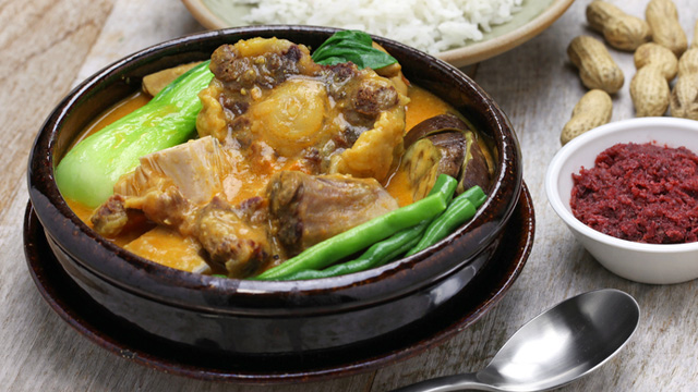 oxtail and beef shank kare-kare served in a black clay pot with rice and bagoong on the side