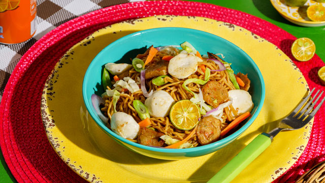 pancit cacnton topped with squid balls and kikiam on a colorful table setting