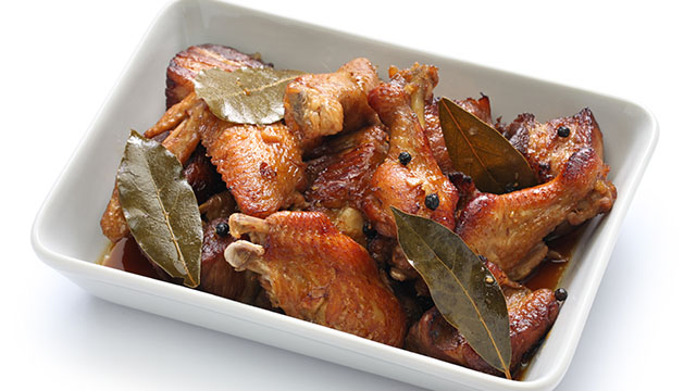 Chicken adobo with whole peppers and laurel leaves in a rectangular serving platter