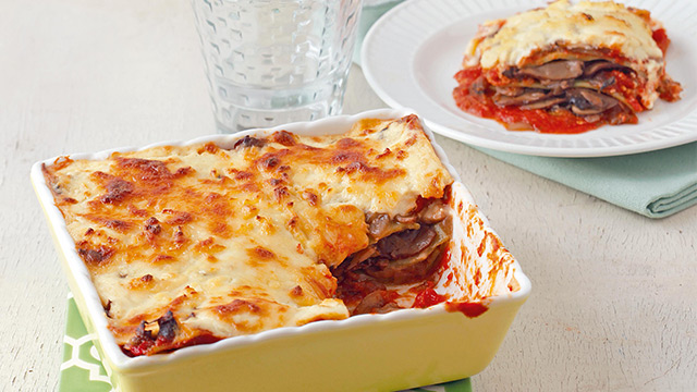 meatless lasagna in a yellow rectangular bowl with a slice taken out of it and the mushroom filling is spilling out